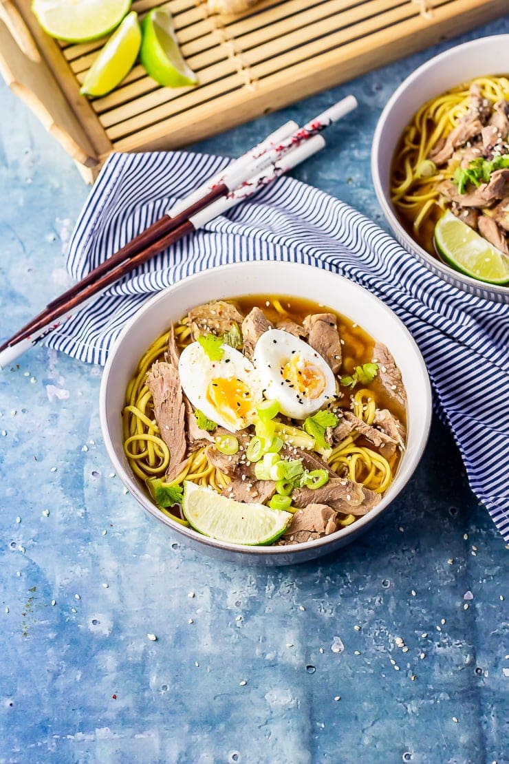 Bowl of leftover turkey soup with noodles on a blue background with a striped cloth