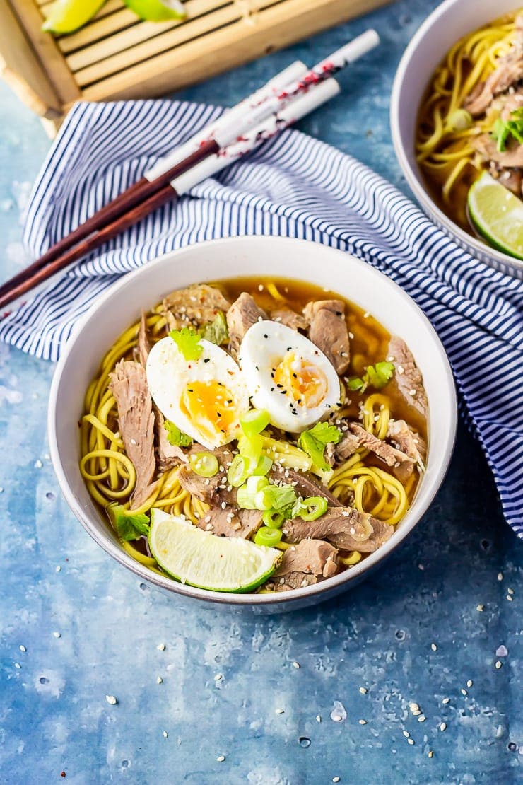 Bowl of leftover turkey soup with noodles on a blue background with a striped cloth