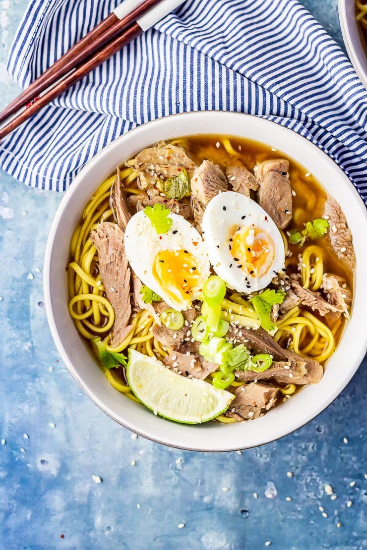 Overhead shot of leftover turkey ramen topped with an egg on a blue background with a striped cloth