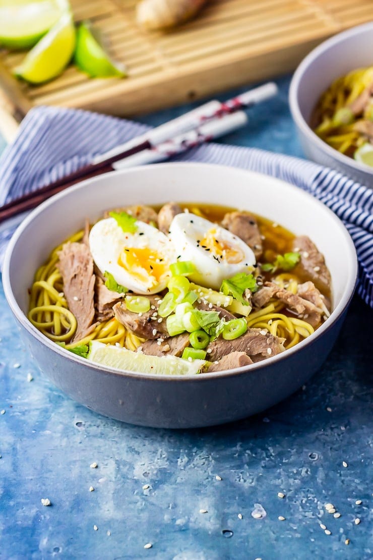 Bowl of leftover turkey soup with noodles topped with an egg on a blue background 