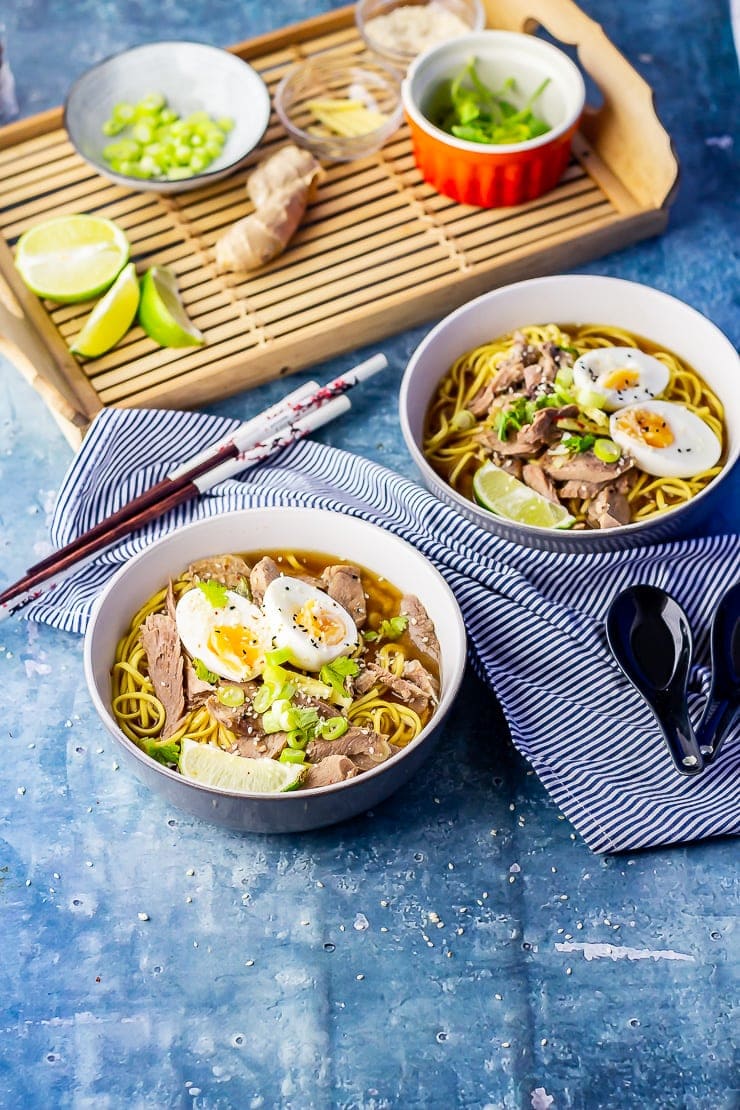 Two bowls of leftover turkey soup with noodles on a blue background with aromatics in the background