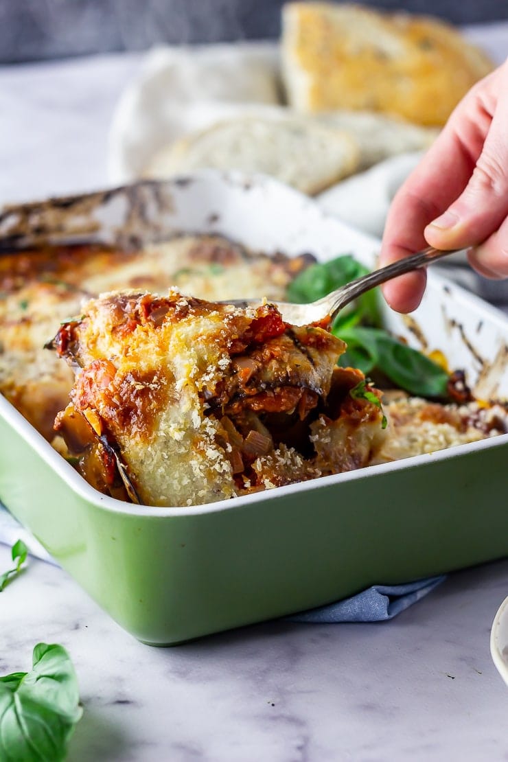 Aubergine parmigiana in a green baking dish with a spoonful being taken