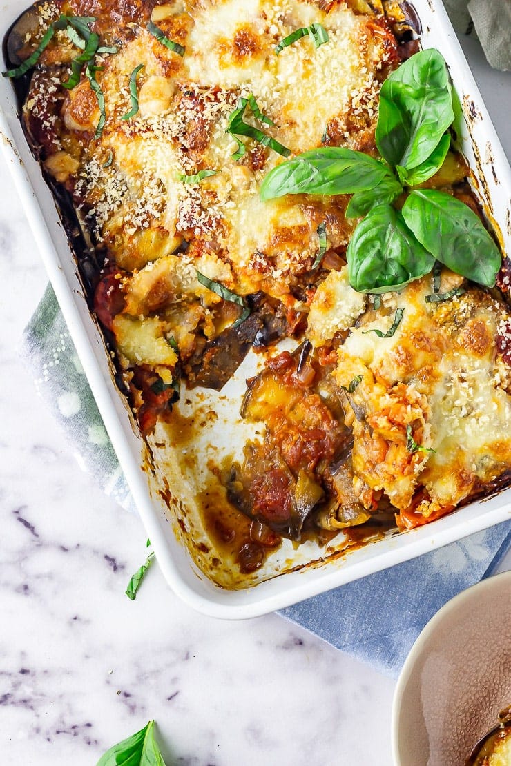 Overhead shot of aubergine parmigiana with a portion taken on a marble background