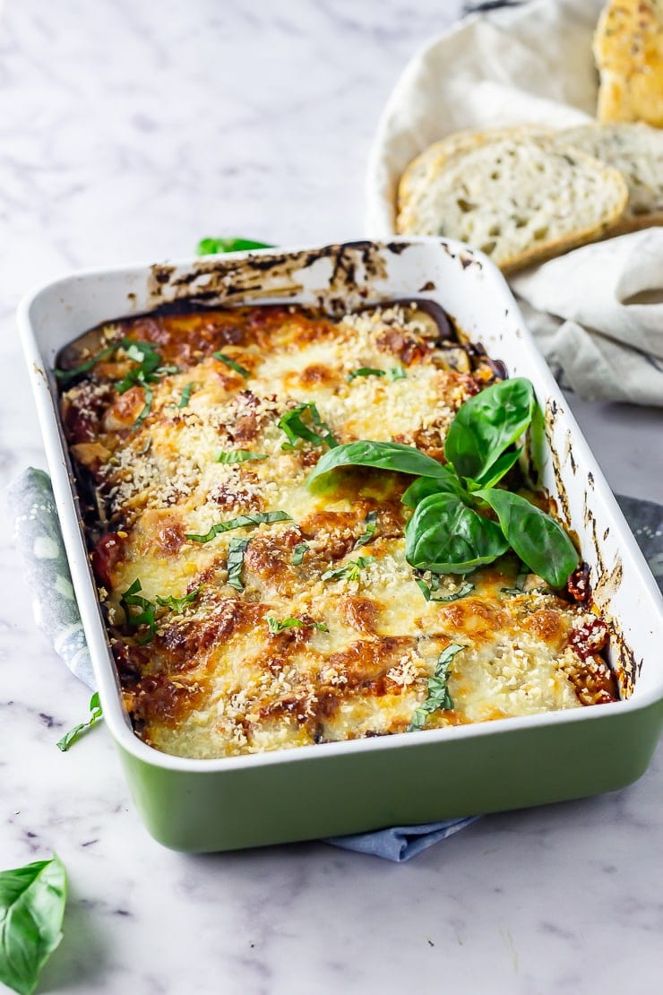 Aubergine parmigiana in a green baking dish on a marble background