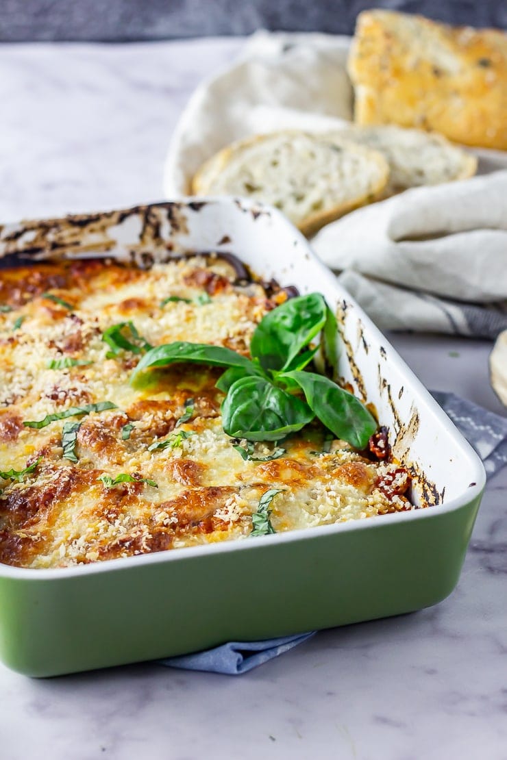 Aubergine parmigiana in a green baking dish on a marble background