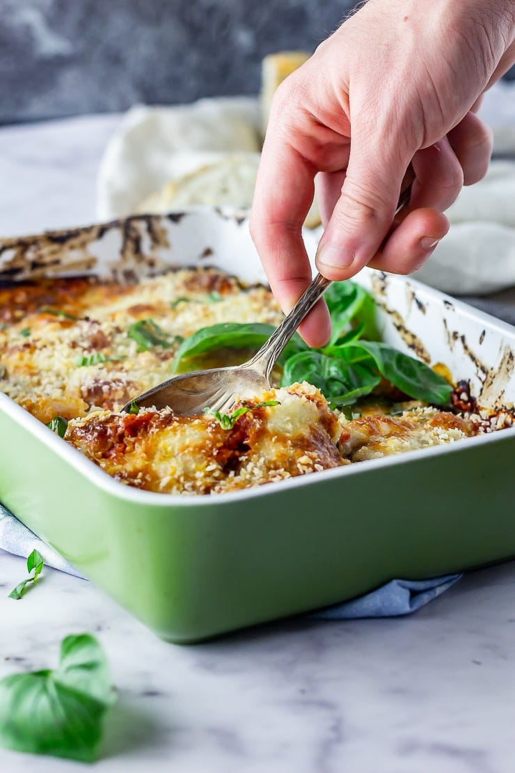 Side on shot of aubergine parmigiana in a green baking dish with a spoonful being taken
