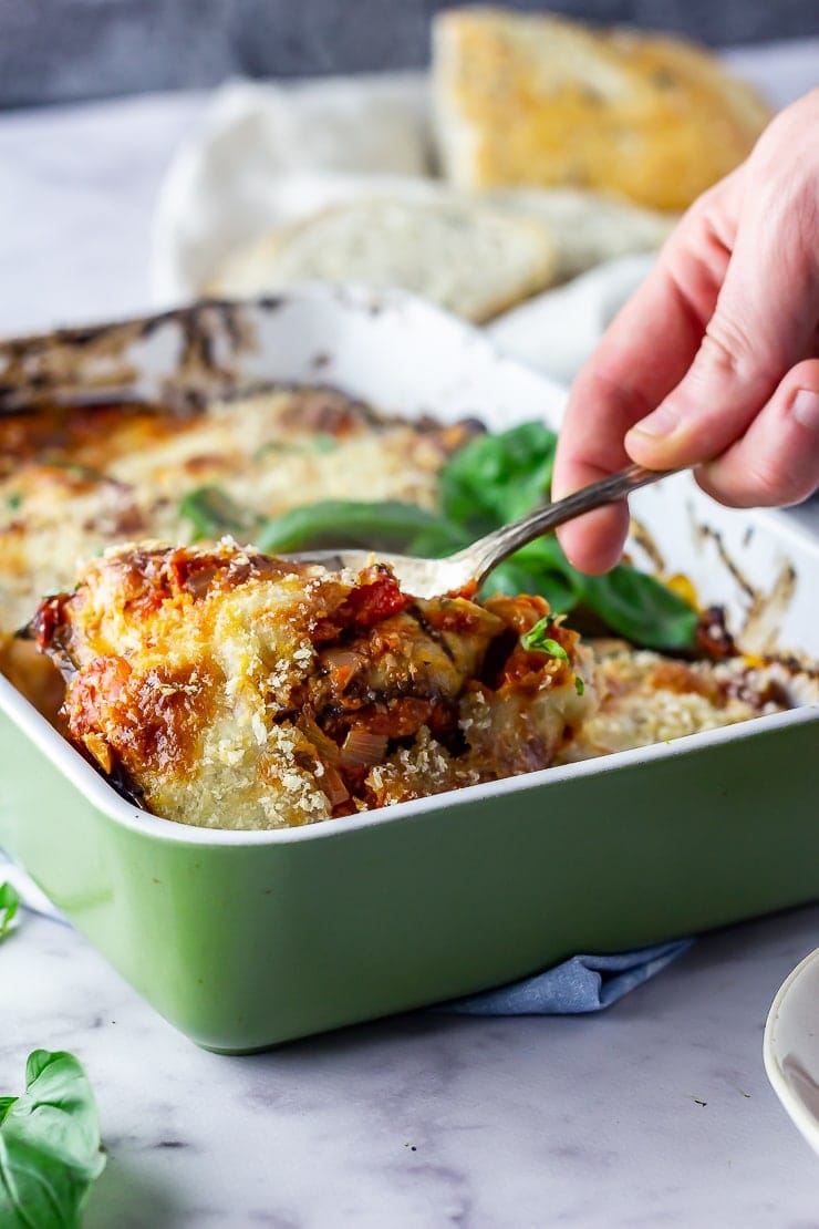 Aubergine parmigiana in a green baking dish with a spoonful being taken