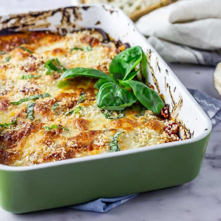 Green baking dish of aubergine parmigiana on a marble background