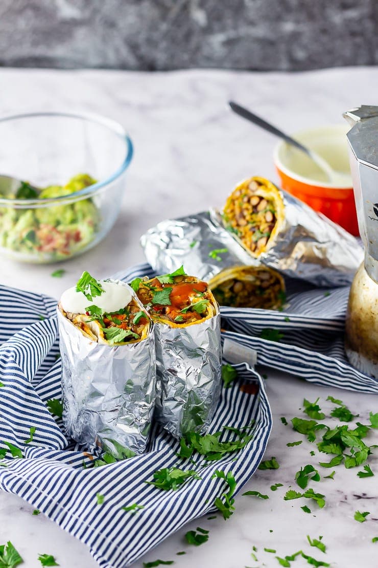 Vegetarian breakfast burrito on a striped cloth and wrapped in foil on a marble background