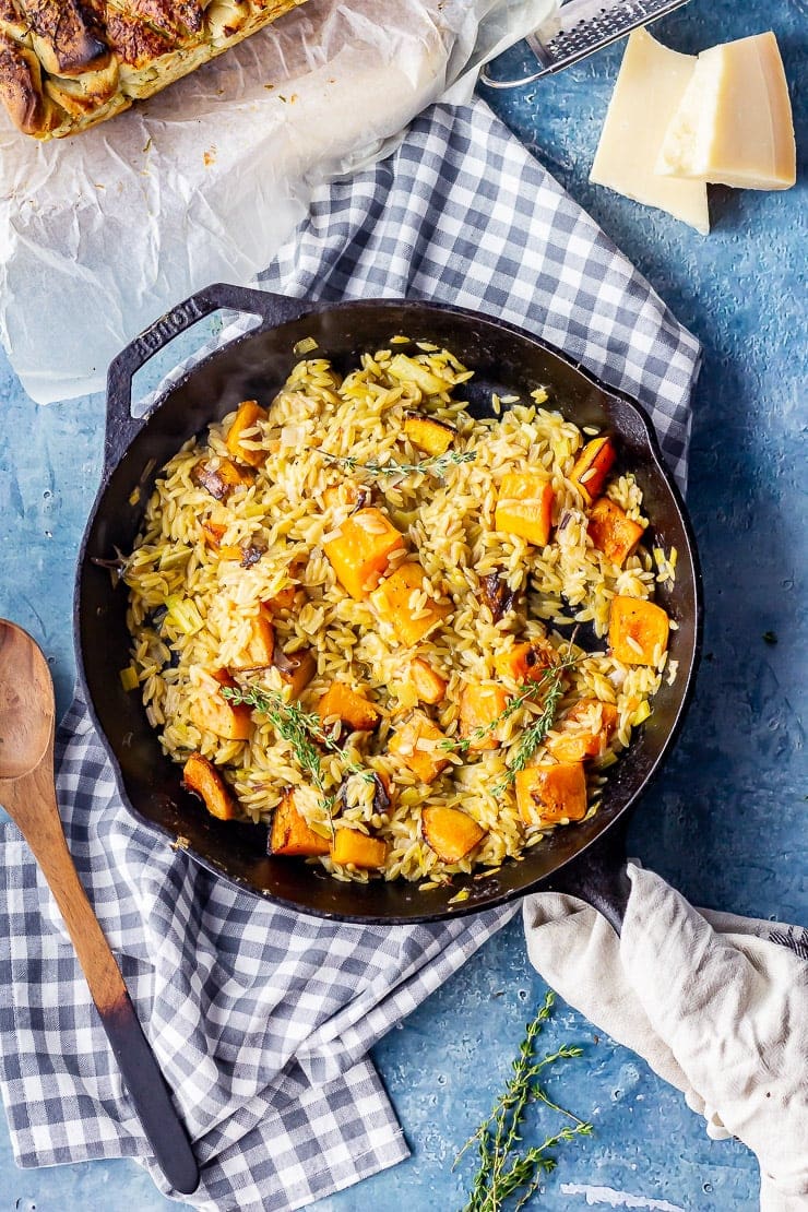 Overhead shot of one pot orzo with butternut squash on a checked cloth over a blue background