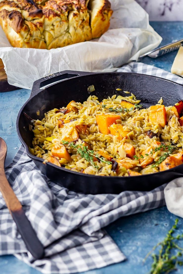 One pot orzo in a cast iron skillet with roasted butternut squash on a checked cloth