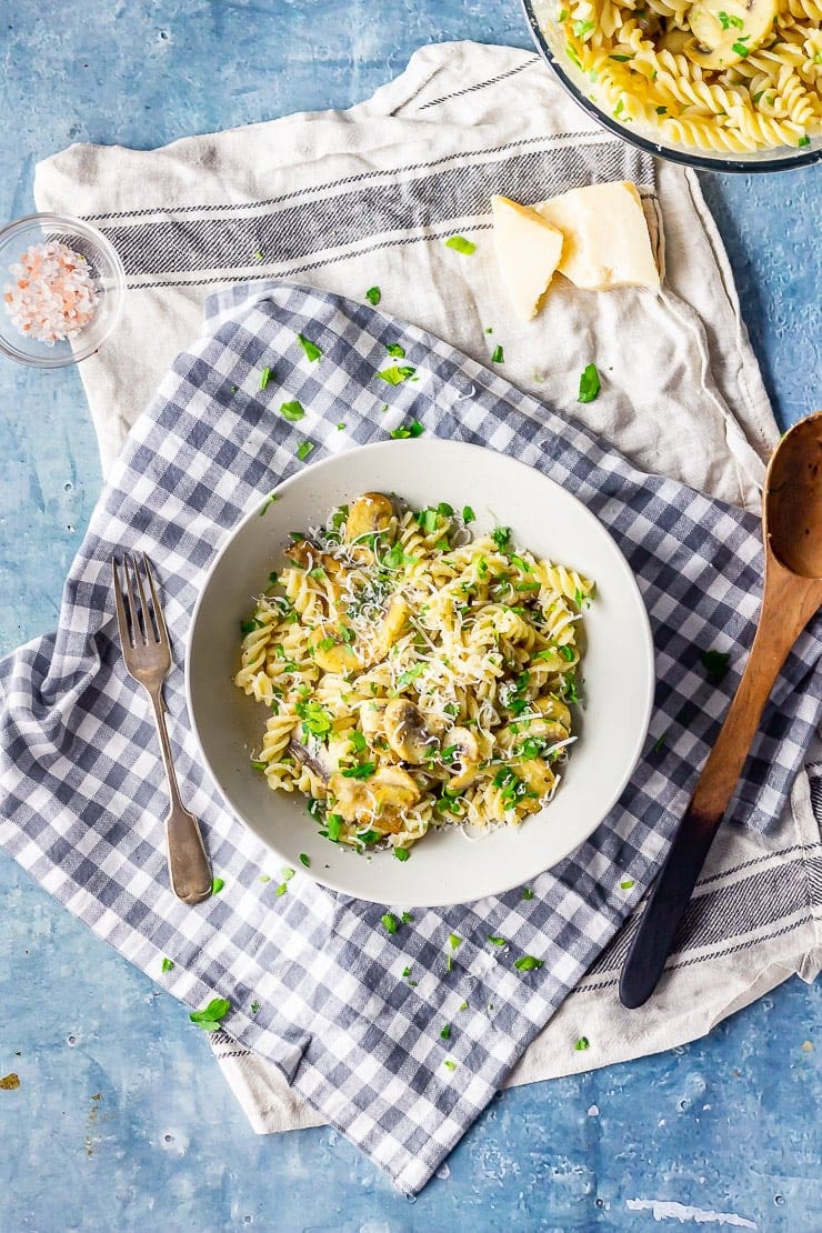 Overhead shot of mushroom pasta on a checked cloth with parmesan