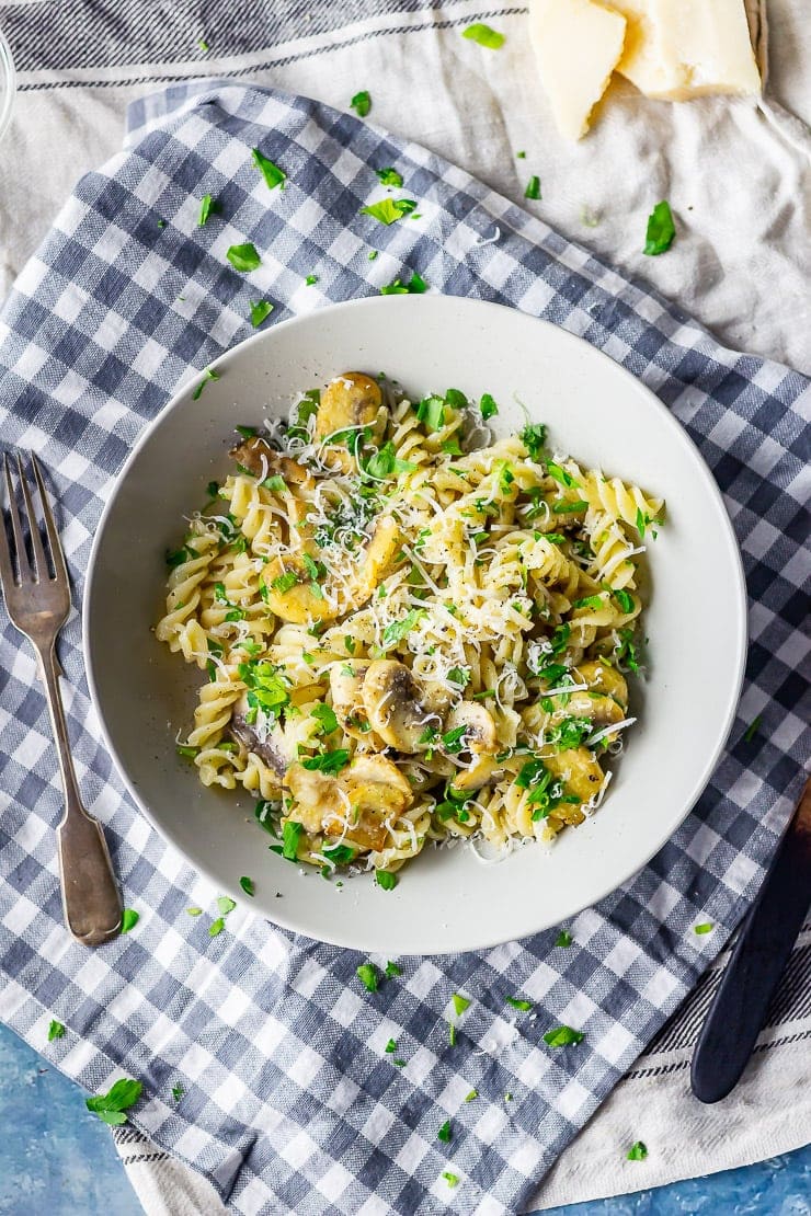 Overhead shot of mushroom pasta on a checked cloth with parmesan