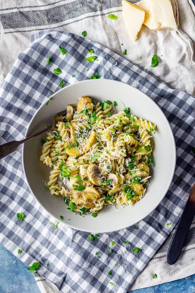 Overhead shot of mushroom pasta on a checked cloth with parmesan