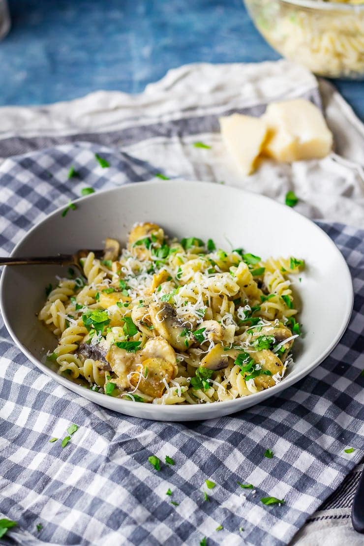 Bowl of garlic mushroom pasta on a checked cloth with parmesan 