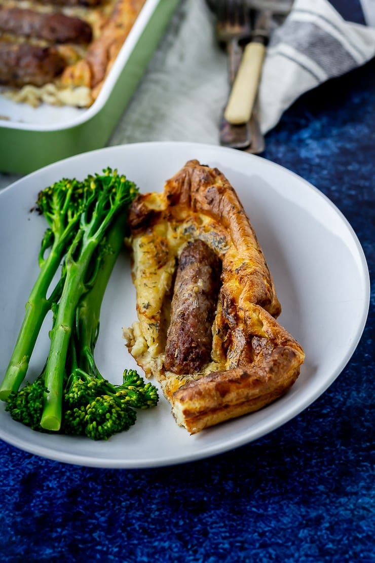 Vegetarian toad in the hole portion in a white bowl with greens on a dark blue background