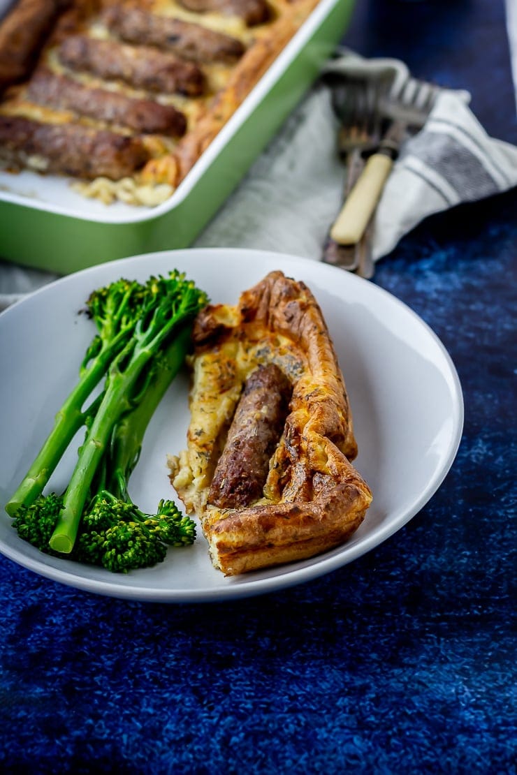 Side shot of a portion of vegetarian toad in the hole in a white bowl on a blue background
