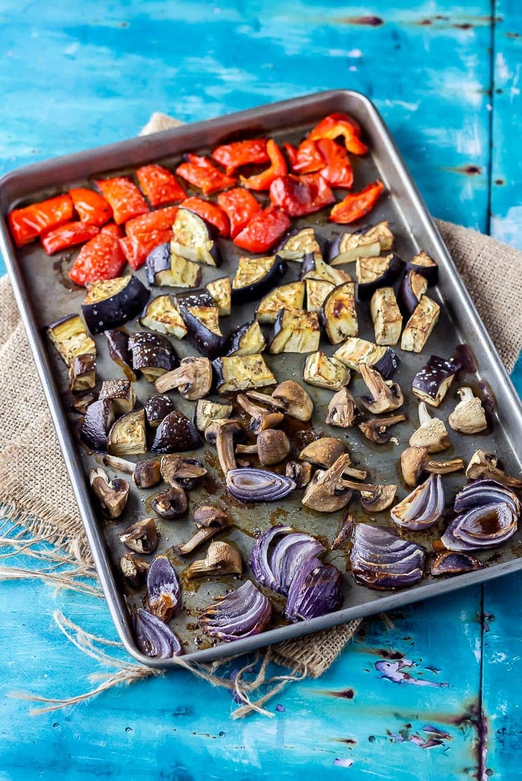 Sheet pan of roasted vegetables for calzones on a blue background