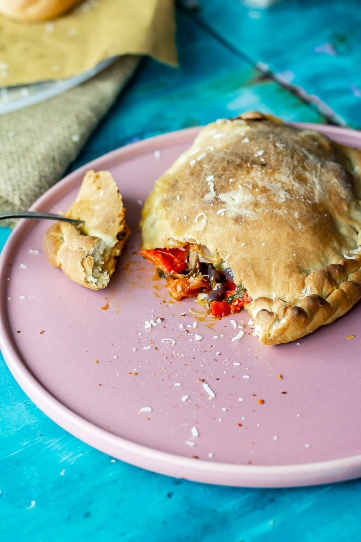 Vegetable calzone on a pink plate with a piece taken and a fork