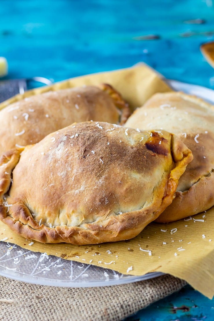 Three roasted vegetables calzones on a plate covered in paper on a blue background