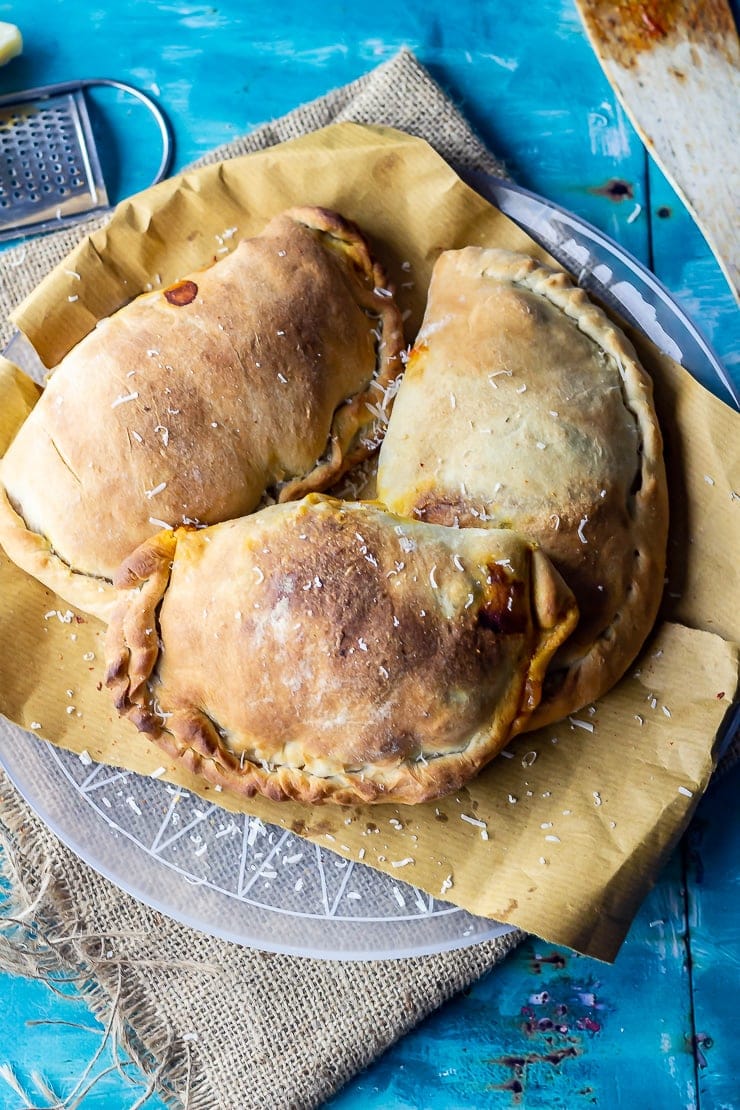 Three roasted vegetable calzones on a plate on a mat over a blue background