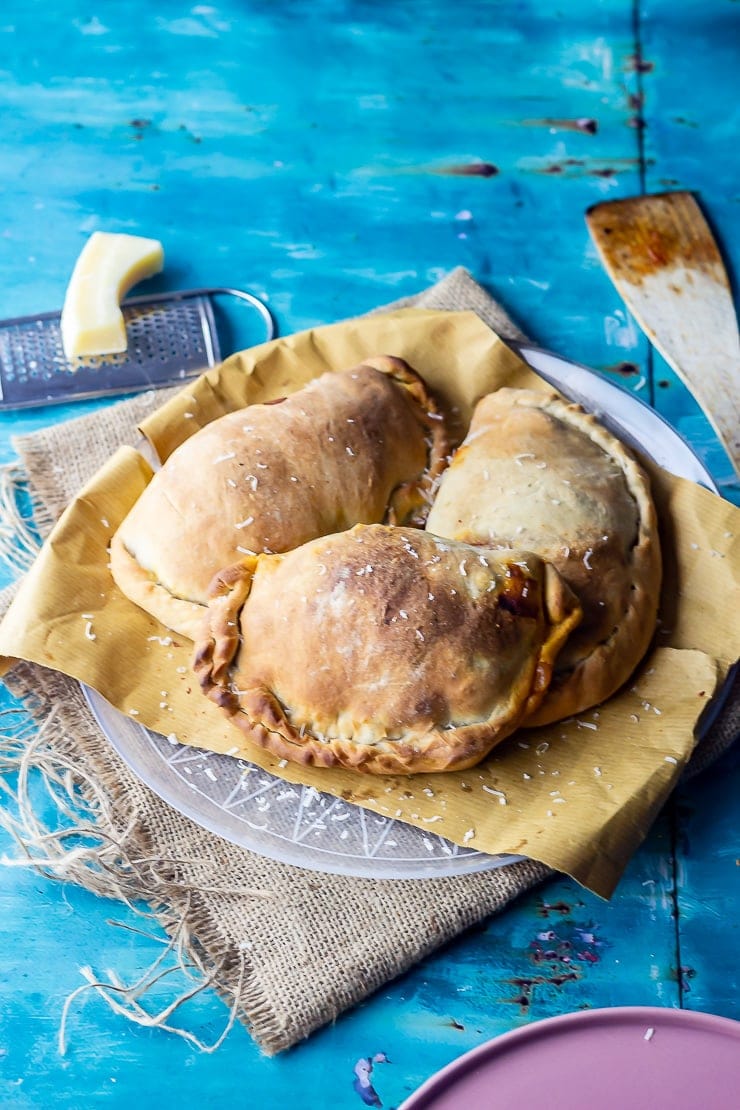 Three calzones on a plate over a mat on a blue background