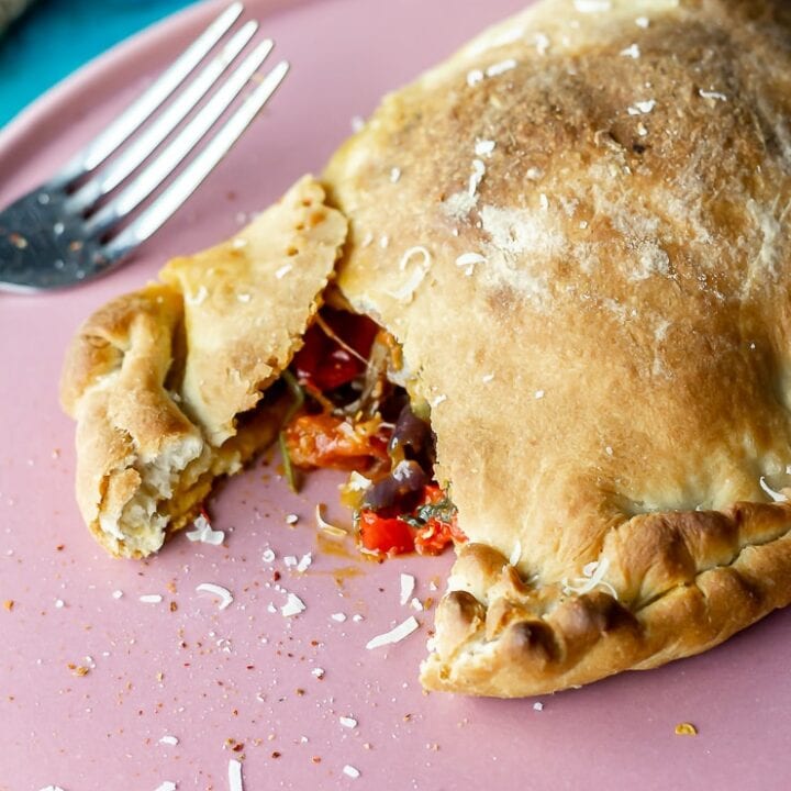 Pink plate with a roasted vegetable calzone and a fork