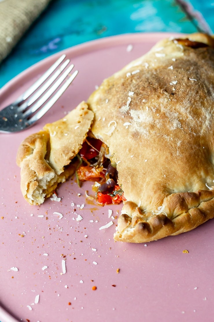 Pink plate with a roasted vegetable calzone and a fork