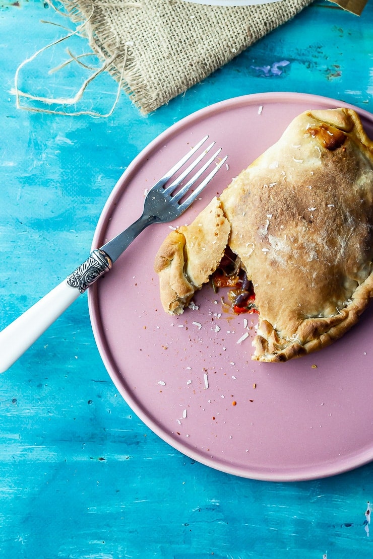 Roasted vegetable calzone on a pink plate with a piece cut open