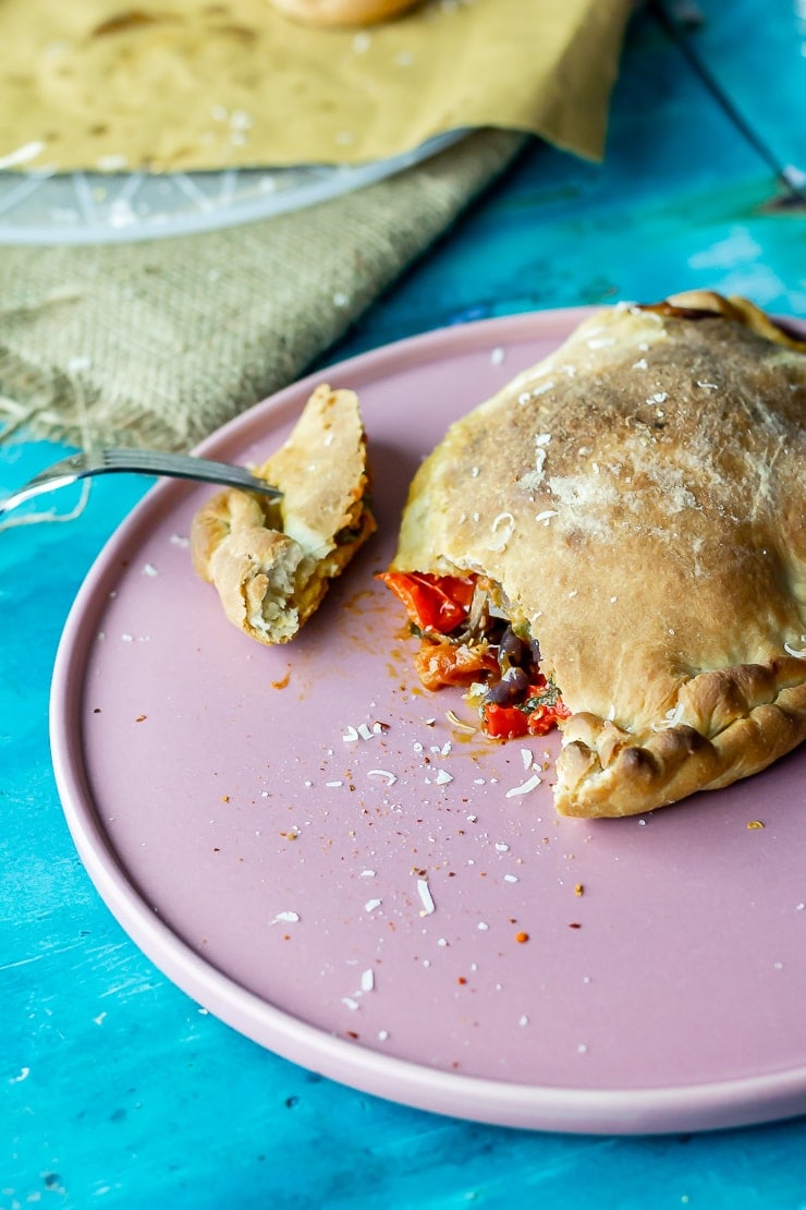 Roasted vegetable calzone on a pink plate with a fork taking a bite