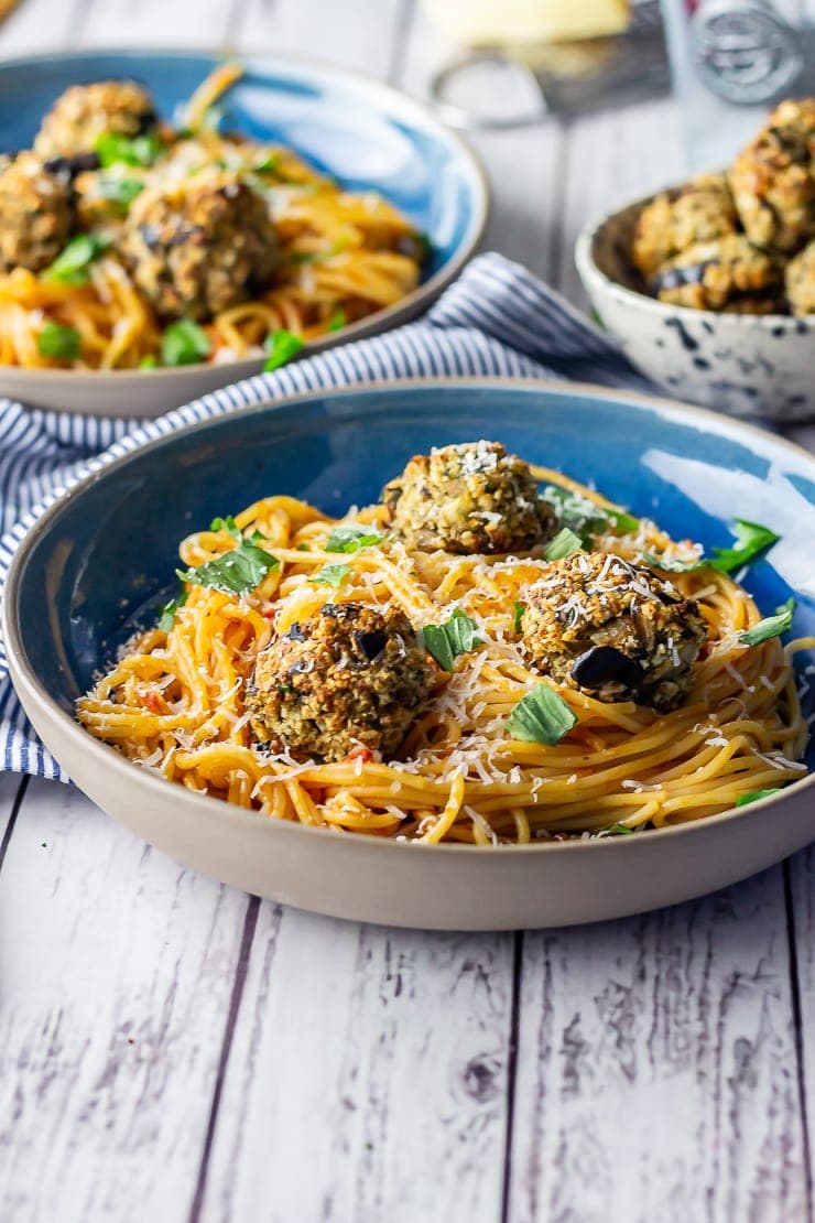 Side on shot of a blue bowl of vegetarian spaghetti and meatballs on a white wooden background