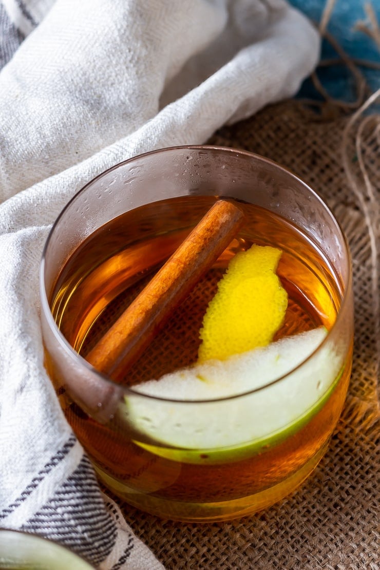 Overhead shot of spiced apple cocktail with rum on a hessian mat with a cloth