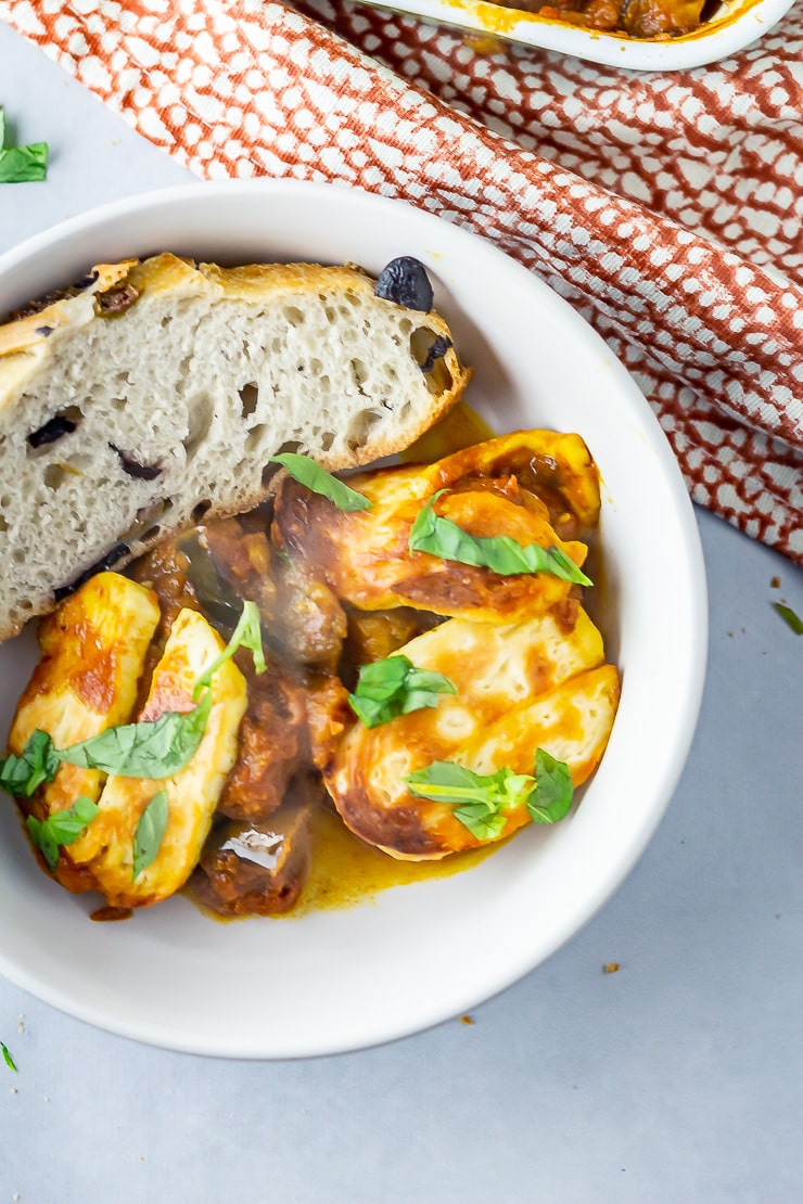 Overhead shot of a bowl of halloumi bake with bread on a grey background