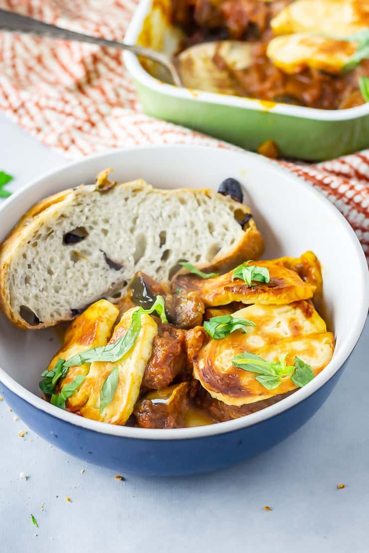 Blue bowl of halloumi bake with bread on a marble background