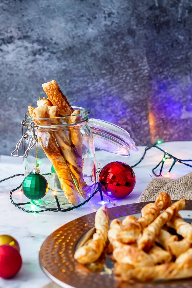 Side on shot of chipotle cheese twists on a platter and in a glass jar with Christmas decorations