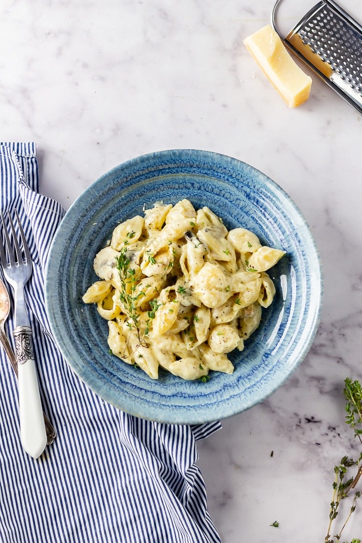 Overhead shot of creamy mushroom pasta in a blue bowl on a marble background