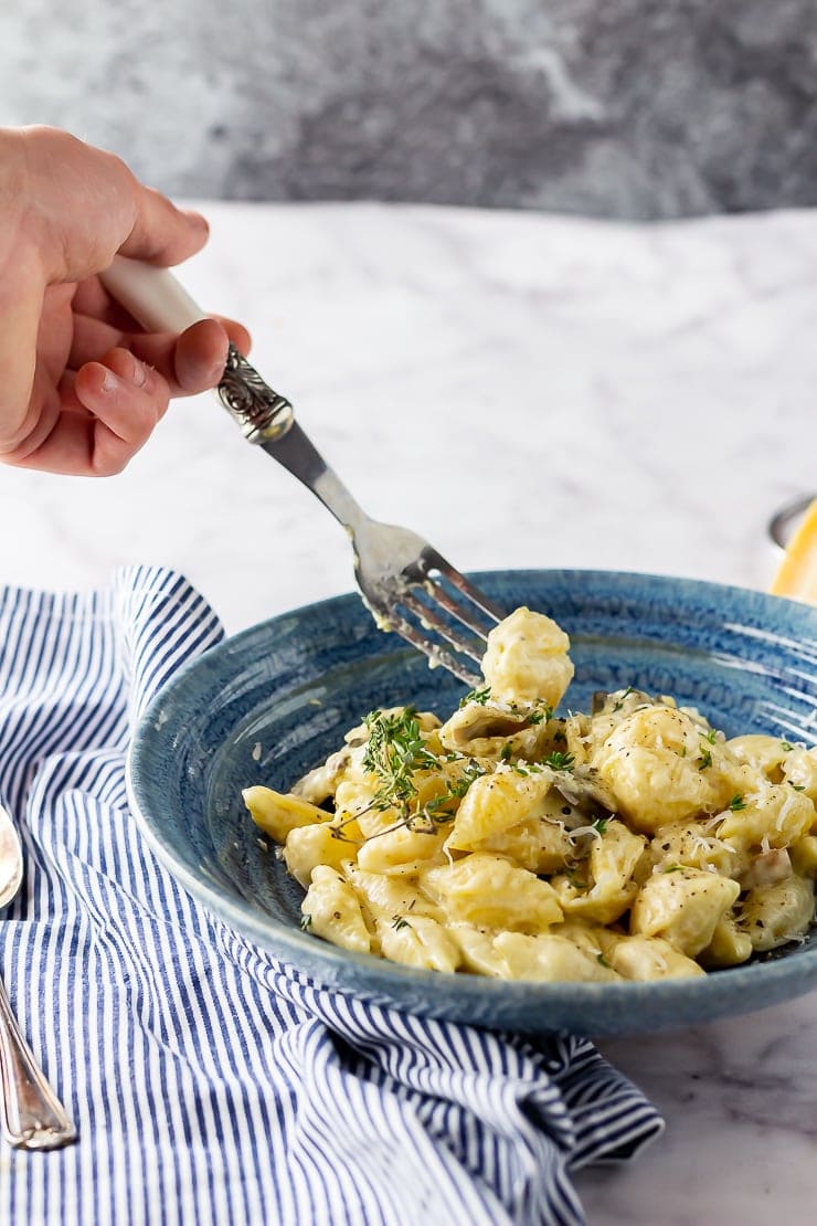 Side shot of a blue bowl of creamy mushroom pasta with a forkful being taken