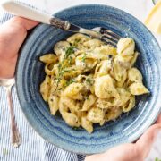 Overhead shot of hands holding a blue bowl of creamy mushroom pasta