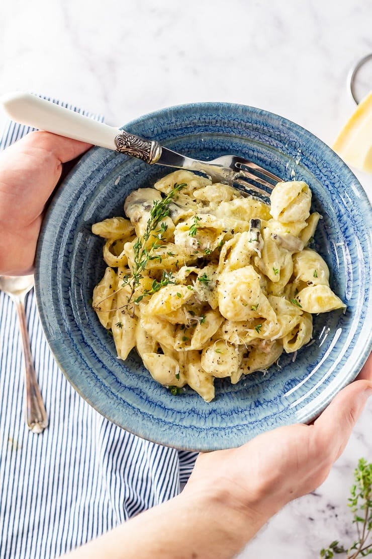 Overhead shot of hands holding a blue bowl of creamy mushroom pasta 