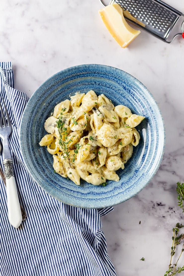 Overhead shot of creamy mushroom pasta in a blue bowl on a marble background