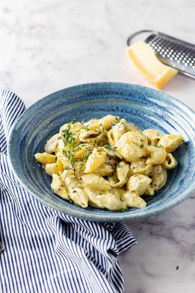 Side angle shot of creamy mushroom pasta in a blue bowl on a marble background