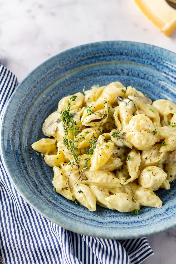 Side angle shot of creamy mushroom pasta in a blue bowl with a striped cloth