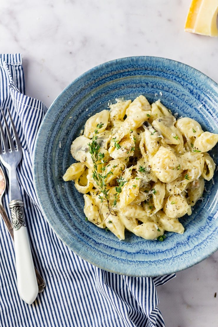 Overhead shot of creamy mushroom pasta in a blue bowl on a marble background