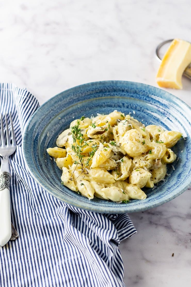 Side angle shot of creamy mushroom pasta in a blue bowl on a striped cloth