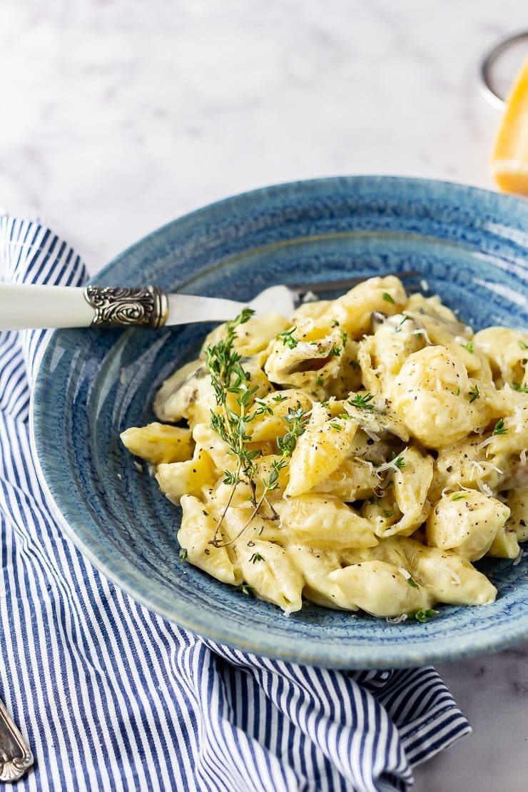 Side angle shot of a blue bowl of creamy mushroom pasta on a striped cloth