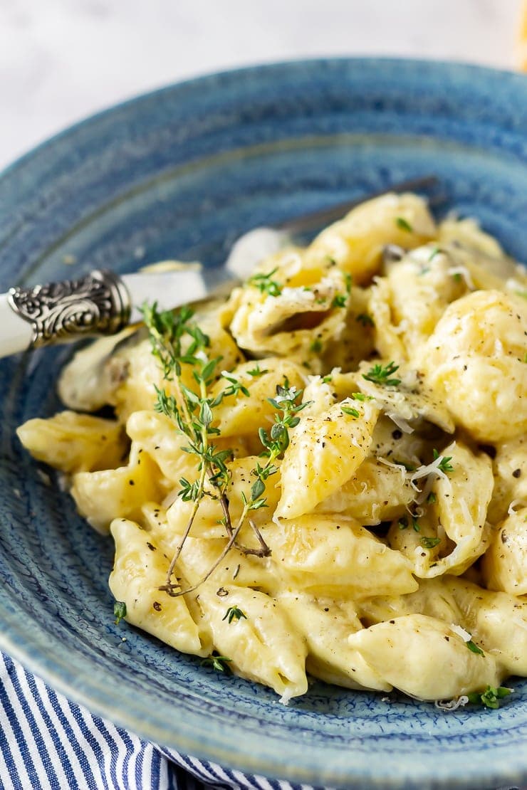 Side angle close up of creamy mushroom pasta in a blue bowl and a fork with thyme sprigs