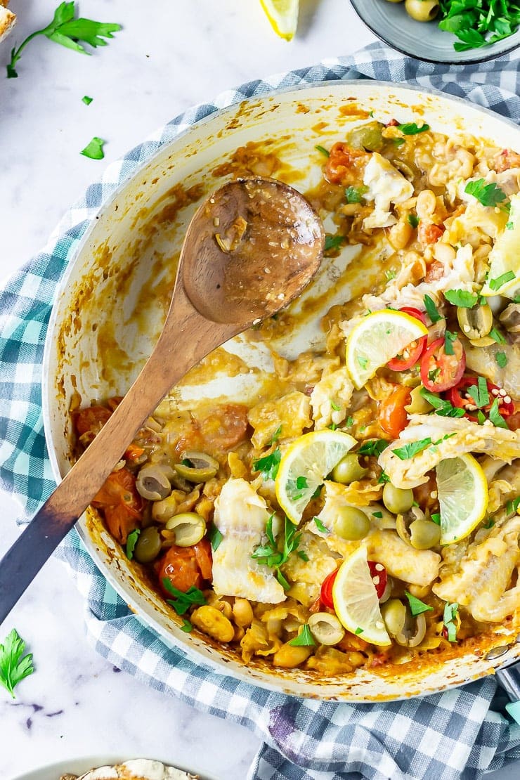 One pot fish stew with a helping taken and a wooden spoon