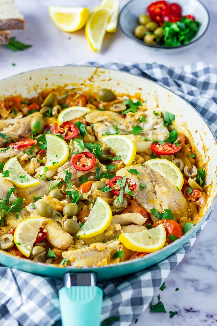 Side angle shot of one pot fish stew in a blue frying pan on a checked cloth