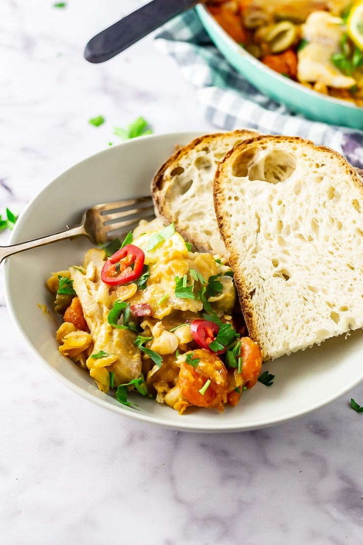 Bowl of one pot fish stew with a fork and bread on a marble background