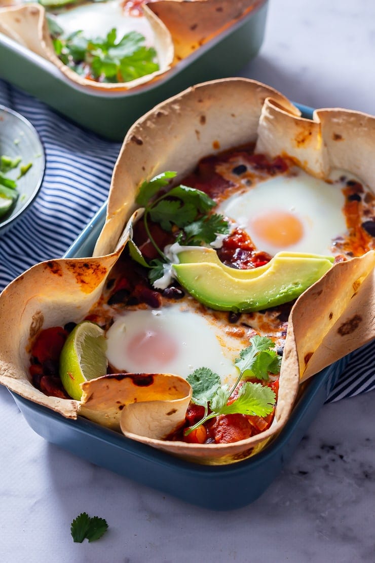 Side angle shot of huevos rancheros baked eggs in a blue dish on a marble background